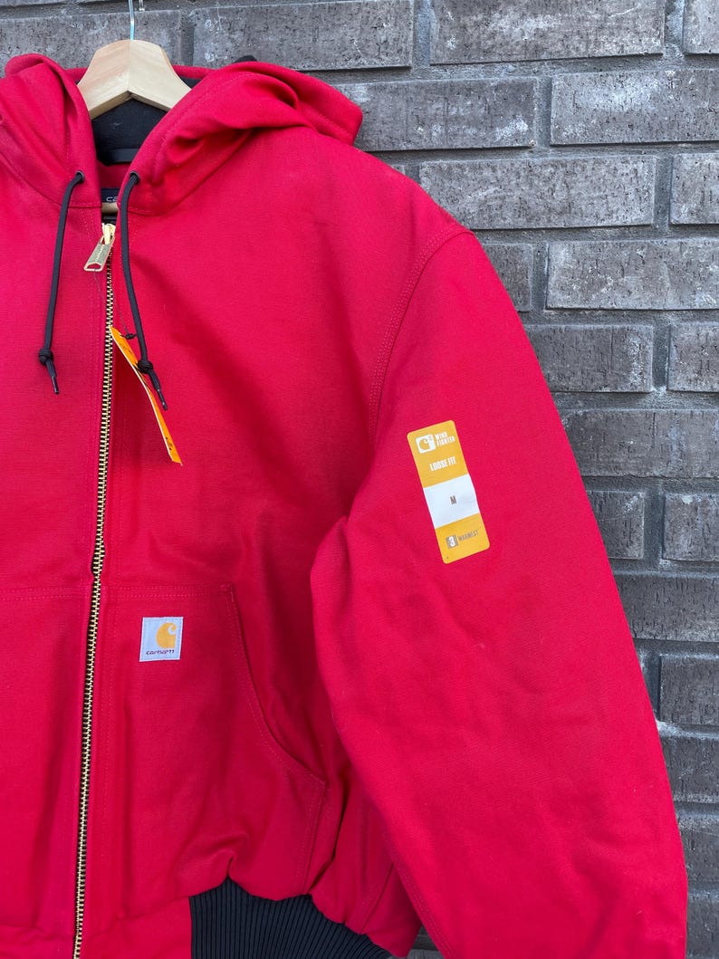 Pode incluir: Casaco vermelho com capuz, z&iacute;per dourado e cord&otilde;es pretos. O casaco tem bainha e punhos canelados pretos. Um pequeno logotipo branco e dourado est&aacute; no bolso frontal. Uma etiqueta amarela est&aacute; anexada.