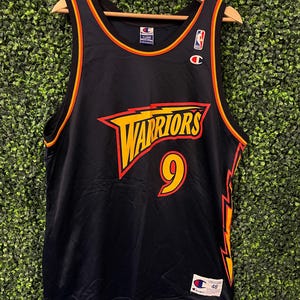 May include: Black Champion Warriors basketball jersey with gold and red accents. The jersey features the word "Warriors" in yellow and red, along with the number "9" in yellow. The jersey is size 48.