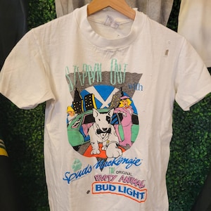 May include: White t-shirt featuring a graphic of a Bull Terrier in a tuxedo, a car, and city skyline. The shirt has the text "Steppin' Out with" and "Spuds MacKenzie The Original Party Animal Bud Light."