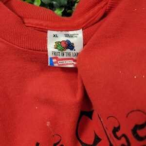 May include: A red XL Fruit of the Loom t-shirt. The tag reads "100% Cotton Preshrunk" and "Made in USA". The shirt has black text on it. The shirt is folded.