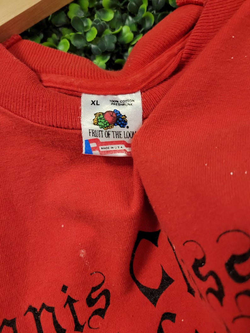 May include: A red XL Fruit of the Loom t-shirt. The tag reads "100% Cotton Preshrunk" and "Made in USA". The shirt has black text on it. The shirt is folded.