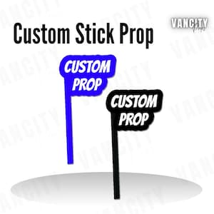 Puede incluir: Se muestran dos accesorios personalizados con forma de palo. Uno es azul con texto blanco y el otro es negro con texto blanco. El texto en ambos dice "CUSTOM PROP". Las palabras "Custom Stick Prop" están escritas encima de los accesorios.