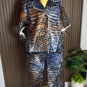 May include: A patterned two-piece pyjama set. The set includes a button-down shirt with short sleeves and matching trousers. The fabric has a design in shades of blue, orange, and black, with white trim. The pyjamas are displayed on a mannequin.