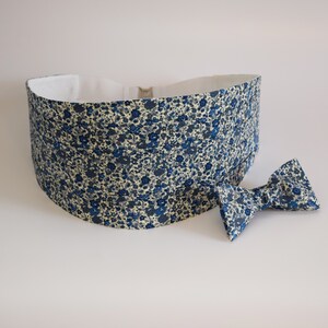 May include: A blue floral cummerbund and matching bow tie set. The fabric features a pattern of small blue flowers on a cream background. The cummerbund is wide and has a white interior lining. The bow tie is pre-tied.