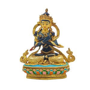 May include: A detailed statue of a seated deity with crossed arms, featuring gold, blue, and red accents. The figure wears a crown and is seated on a decorative base with floral patterns. The statue has a serene expression.