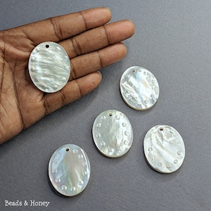May include: Five white oval-shaped mother of pearl pendants with a hole at the top for stringing. Each pendant has a circular pattern of small white dots around the edge.