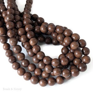 May include: Close-up of strands of dark brown wooden beads. The beads are round and have a smooth, polished finish. The beads are strung together, creating a flowing, organic shape. The beads are a natural, earthy color.