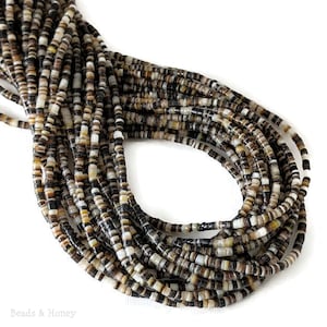May include: Strands of small, flat beads in a mix of colors including black, brown, and cream. The beads are strung together, forming a coiled shape. The beads appear to be made of natural materials, possibly shell or stone.