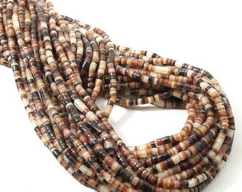May include: A long strand of small, cylindrical beads in varying shades of brown, tan, cream, and black. The beads are arranged in a dense, multi-layered loop, showcasing a smooth, polished texture and a repeating pattern of earthy, neutral tones.