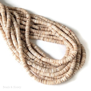 May include: A pile of beige and tan shell beads, strung together, creating a layered effect. The beads are flat, circular, and have a natural, organic appearance. The image is well-lit, highlighting the texture and color variations of the beads. The words "Beads & Honey" are at the bottom.