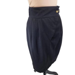 Op de afbeelding: Een zwarte rok met een hoge taille en een geplooide voorkant. De rok heeft een gouden knoopsluiting aan de taille.