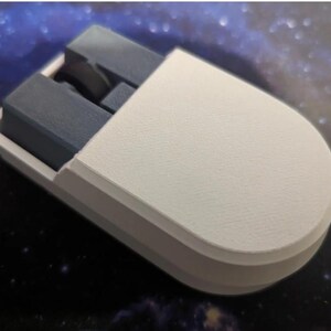 Puede incluir: Un objeto blanco y gris impreso en 3D con forma redondeada. El objeto tiene una carcasa exterior blanca y componentes internos grises. El dise&ntilde;o parece ser un art&iacute;culo personalizado, posiblemente un accesorio o componente &uacute;nico.