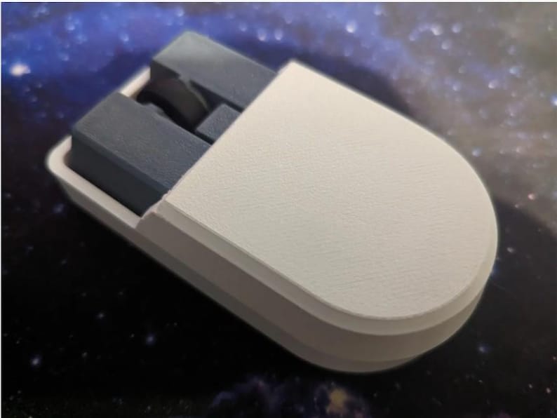 Puede incluir: Un objeto blanco y gris impreso en 3D con forma redondeada. El objeto tiene una carcasa exterior blanca y componentes internos grises. El dise&ntilde;o parece ser un art&iacute;culo personalizado, posiblemente un accesorio o componente &uacute;nico.
