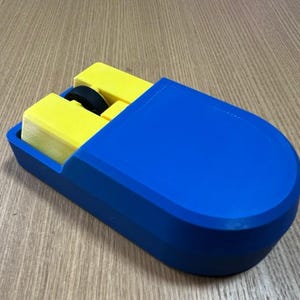 Puede incluir: Un rat&oacute;n azul y amarillo impreso en 3D. El rat&oacute;n tiene una carcasa exterior azul con un interior amarillo. La rueda de desplazamiento es negra. El rat&oacute;n est&aacute; dise&ntilde;ado con una forma rectangular y bordes redondeados.
