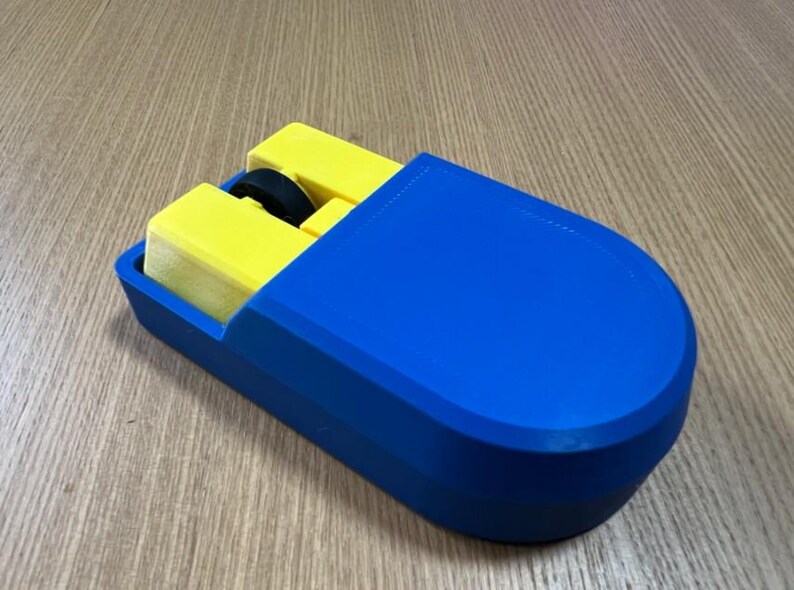 Puede incluir: Un rat&oacute;n azul y amarillo impreso en 3D. El rat&oacute;n tiene una carcasa exterior azul con un interior amarillo. La rueda de desplazamiento es negra. El rat&oacute;n est&aacute; dise&ntilde;ado con una forma rectangular y bordes redondeados.