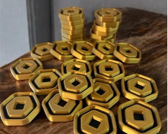 May include: A collection of gold-colored, hexagonal tokens with a black square center. Some tokens are stacked, while others are scattered on a wooden surface. The tokens have a three-dimensional design, suggesting they are game pieces or decorative items.