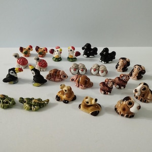 Op de afbeelding: Een verzameling van drieëntwintig miniatuur keramische dierenbeeldjes, waaronder toekans, schildpadden, kippen, krokodillen en diverse honden. Elk klein, handbeschilderd figuurtje heeft opvallende kleuren en gedetailleerde gelaatstrekken met een glanzende afwerking.