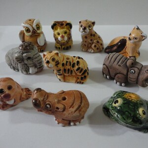 Puede incluir: Una colección de diez pequeñas figuritas de animales de cerámica, que incluyen una rana, un hipopótamo, un rinoceronte, un tigre, un leopardo, un búho y una foca. Las figuritas están pintadas en varios colores, incluyendo verde, marrón, negro, blanco y naranja.