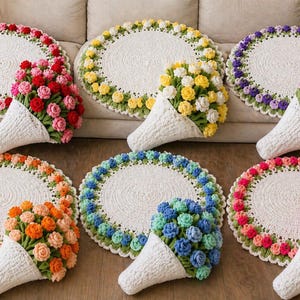May include: A collection of six handmade crochet rugs with floral accents. Each rug features a white center, a scalloped green border, and a ring of colorful crochet flowers. Accompanying each rug is a matching crochet flower bouquet in a white cone.