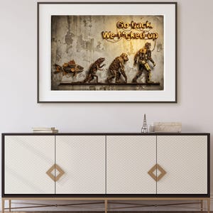Puede incluir: Obra de arte enmarcada que representa una progresión evolutiva de pez a figura robótica. El texto "Go back. We f*cked up" se muestra en letras doradas. La obra está montada sobre un mueble blanco y negro con detalles dorados.