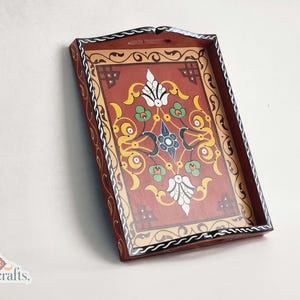 May include: Rectangular wooden tray with a decorative floral design. The tray features a red background with a central floral pattern in white, green, and blue. The border is brown with black and white accents. The logo "tislitercrafts," is in the bottom left corner.