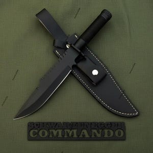 May include: A black survival knife with a serrated blade and a black handle, resting in a black leather sheath. The knife is labeled "SCHWARZENEGGER COMMANDO" in a black, raised font.