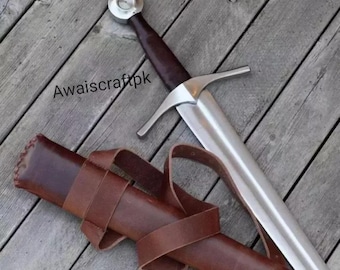 May include: A medieval-style sword with a polished steel blade and a brown leather-wrapped handle. The sword features a crossguard and a circular pommel. A brown leather sheath with a belt is also included. The text "Awaiscraftpk" is visible.