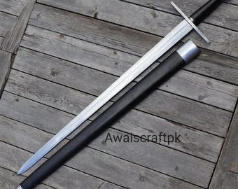 May include: A long, silver sword with a black handle and crossguard, resting on a wooden surface. The sword is partially sheathed in a black scabbard with silver accents. The text "Awaiscraftpk" is visible.
