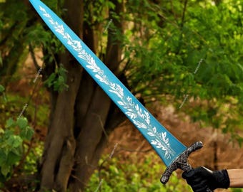 Puede incluir: Una espada larga y azul con un diseño floral blanco a lo largo del borde de la hoja. La empuñadura tiene un diseño oscuro y texturizado. La espada se muestra sobre un fondo de follaje verde.