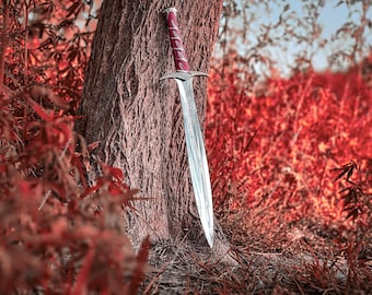 May include: A silver sword with a burgundy handle leans against a tree trunk. The sword has a long, pointed blade and a decorative hilt. The background features red foliage and a blurred sky, creating a fantasy or medieval theme.
