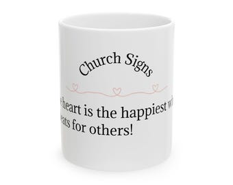 Puede incluir: Taza de cerámica blanca con el texto "Church Signs" en escritura negra. Debajo, un diseño de corazón rosa y la cita "¡El corazón es el más feliz cuando late por los demás!"