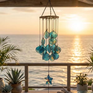 May include: A hanging wind chime with turquoise-colored, shell-shaped accents and a star-shaped pendant. The chime is suspended from a chain and hangs against a backdrop of the ocean and sunset. The wind chime is a decorative outdoor item.