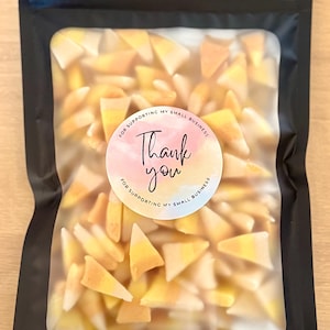 May include: A black, resealable bag filled with candy corn. A round sticker on the bag reads "Thank you" in cursive, with the text "For supporting my small business" around the edge. The candy corn is yellow, orange, and white.