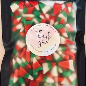 May include: A black cellophane bag filled with red, green, and white candy corn. A round sticker on the bag says "Thank you" in cursive script, with "For supporting my small business" around the edge.