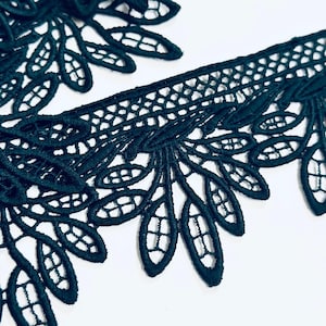 Può includere: Primo piano di un bordo in pizzo verde scuro con un motivo a foglie floreali. Il pizzo presenta un bordo smerlato con trafori dettagliati e un motivo delicato e intricato. Il bordo viene probabilmente utilizzato per cucire, creare o abbellire capi di abbigliamento.