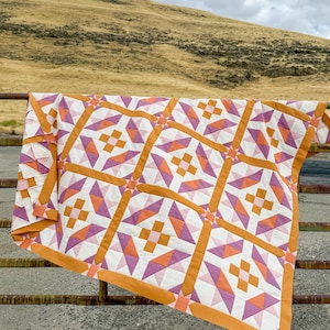Peut inclure: Une courtepointe présentant un motif géométrique répétitif dans des tons d'orange, de rose clair et de violet foncé, séparé par des bandes orange unies. Le design se compose de carrés centraux entourés de triangles et de rectangles sur fond blanc.