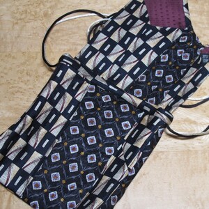 May include: A collection of drawstring bags made from repurposed neckties. The bags feature various patterns, including geometric shapes and floral designs, in shades of navy, beige, and burgundy. The drawstring cords are black and white.