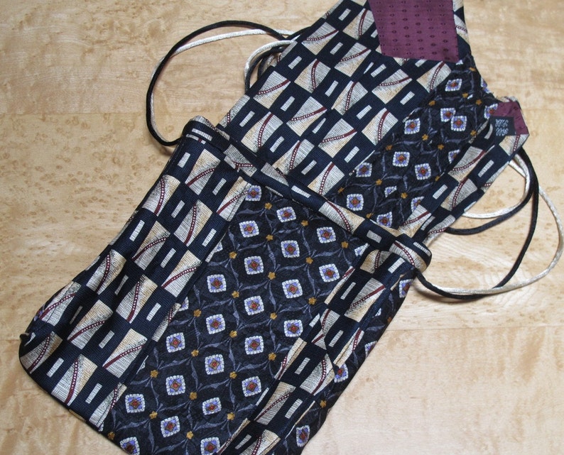 May include: A collection of drawstring bags made from repurposed neckties. The bags feature various patterns, including geometric shapes and floral designs, in shades of navy, beige, and burgundy. The drawstring cords are black and white.