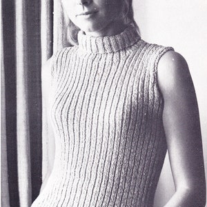 May include: A light beige, sleeveless top with a ribbed knit design and a turtleneck. The vertical ribbing is a prominent feature. The woman is wearing a bracelet. The top is a vintage style.
