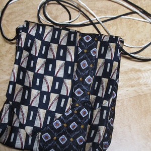 May include: A handmade crossbody bag crafted from repurposed neckties. The bag features a geometric pattern in navy, beige, and burgundy, with a contrasting floral design. It has a black and white cord strap for carrying.