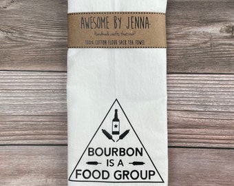 May include: White tea towel with a black triangle design. The triangle contains a bottle of bourbon, wheat stalks, and the text "Bourbon is a Food Group".