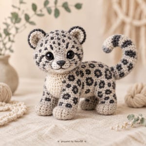 Pode incluir: Um bicho de pelúcia de crochê em forma de filhote de leopardo-das-neves com fio creme, manchas cinza-escuras, olhos pretos grandes e uma cauda curva. O texto "prepared by flexor58" está impresso em letras pretas pequenas na parte inferior.
