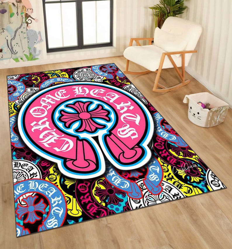 May include: A rectangular area rug with a vibrant, multi-colored design. The rug features a large, pink and white emblem with the words "Chrome Hearts" and a cross-shaped design. The background is filled with various patterns and colors, including blue, yellow, and black.