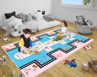 May include: A colorful children's play mat with a hopscotch design, featuring numbers, animals, and the words "Start" and "Finish." The mat is primarily blue and pink, with black borders. Toys are scattered around the mat.