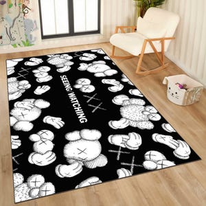 May include: Black rectangular rug featuring a repeating pattern of white cartoon figures with X-shaped eyes and crossbones. The words "SEEING WATCHING" are printed vertically in white.
