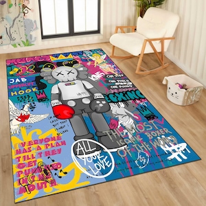 May include: A rectangular area rug with a colorful graffiti design. The rug features a large cartoon figure with boxing gloves, surrounded by text and illustrations. The color palette includes blue, red, black, and white.