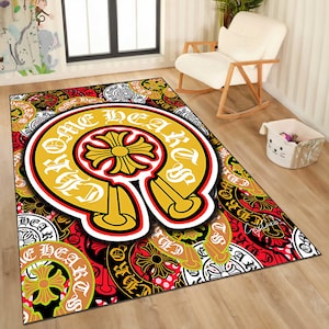 May include: A rectangular area rug with a bold design. The rug features a large, yellow horseshoe shape with the words "Chrome Hearts" in white. The background is a mix of red, black, and white patterns with floral and cross motifs.