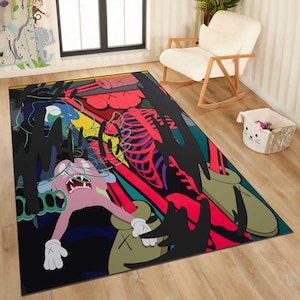 May include: A large rectangular area rug with a colorful, abstract design. The rug features a pink cartoon figure with white gloves, a red skeleton, and black, green, and blue shapes against a black background. The rug is placed on a wooden floor.