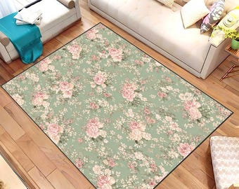 May include: A rectangular area rug with a floral pattern. The rug features a light green background with a repeating pattern of pink and white flowers. The rug is bordered with a thin black line.