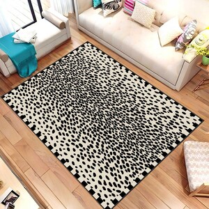 May include: A rectangular area rug with a black and white spotted pattern, resembling a Dalmatian's coat. The rug is placed on a hardwood floor, with a black border. The rug is a home decor item.